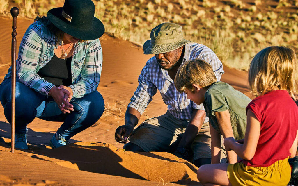 children with their guide looking at wildlife footprints in the sand