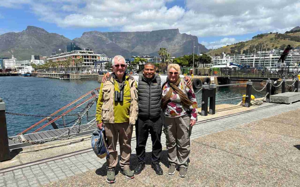 Three people standing together with their arms around each other at a harbour, with mountains in the background in Cape Town.