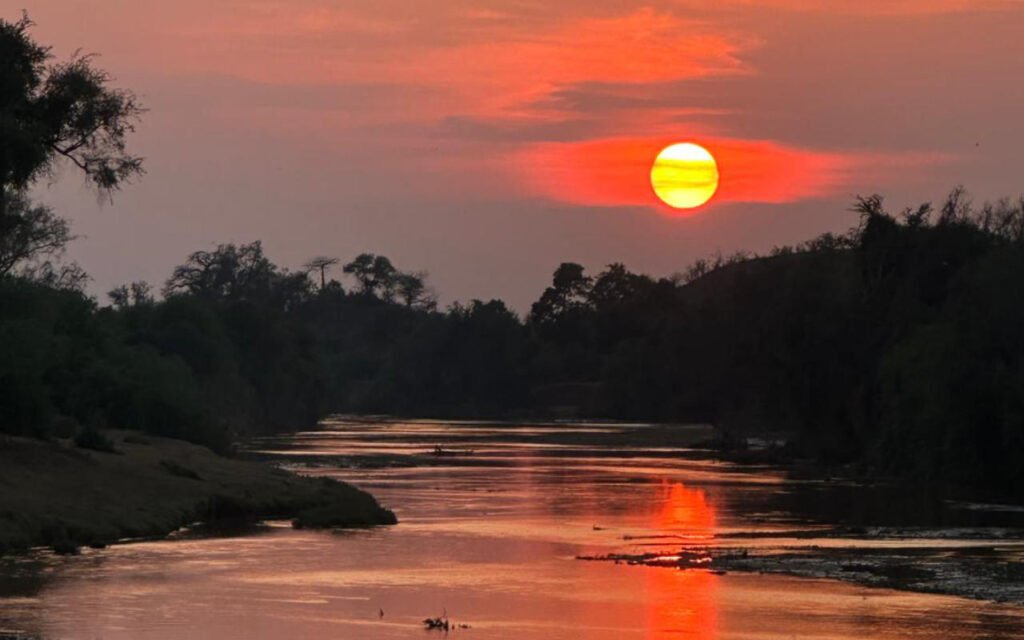 The sun is setting on the horizon above a river in Pafuri.
