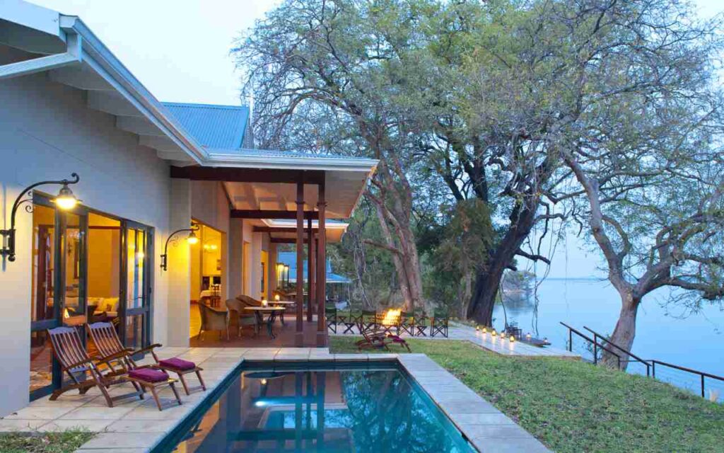 Lodge accommodation under trees, with lounge seating next to a small pool, overlooking a river.